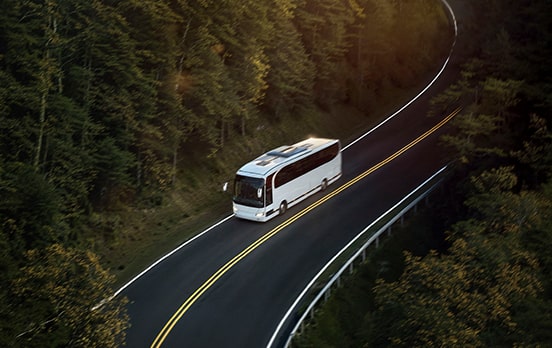 Long distance bus driving on a road surrounded by a forest